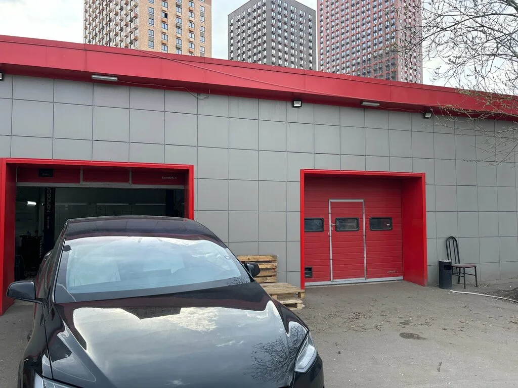 Фасад сервиса Evc Group с открытыми воротами и автомобилем Tesla у въезда.
