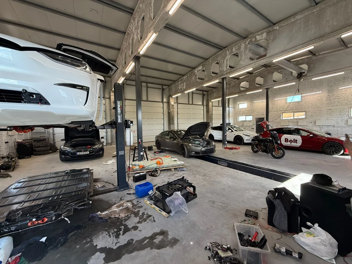 Ремонтный цех EVS Vilnius с несколькими автомобилями Tesla и открытой батареей на переднем плане.