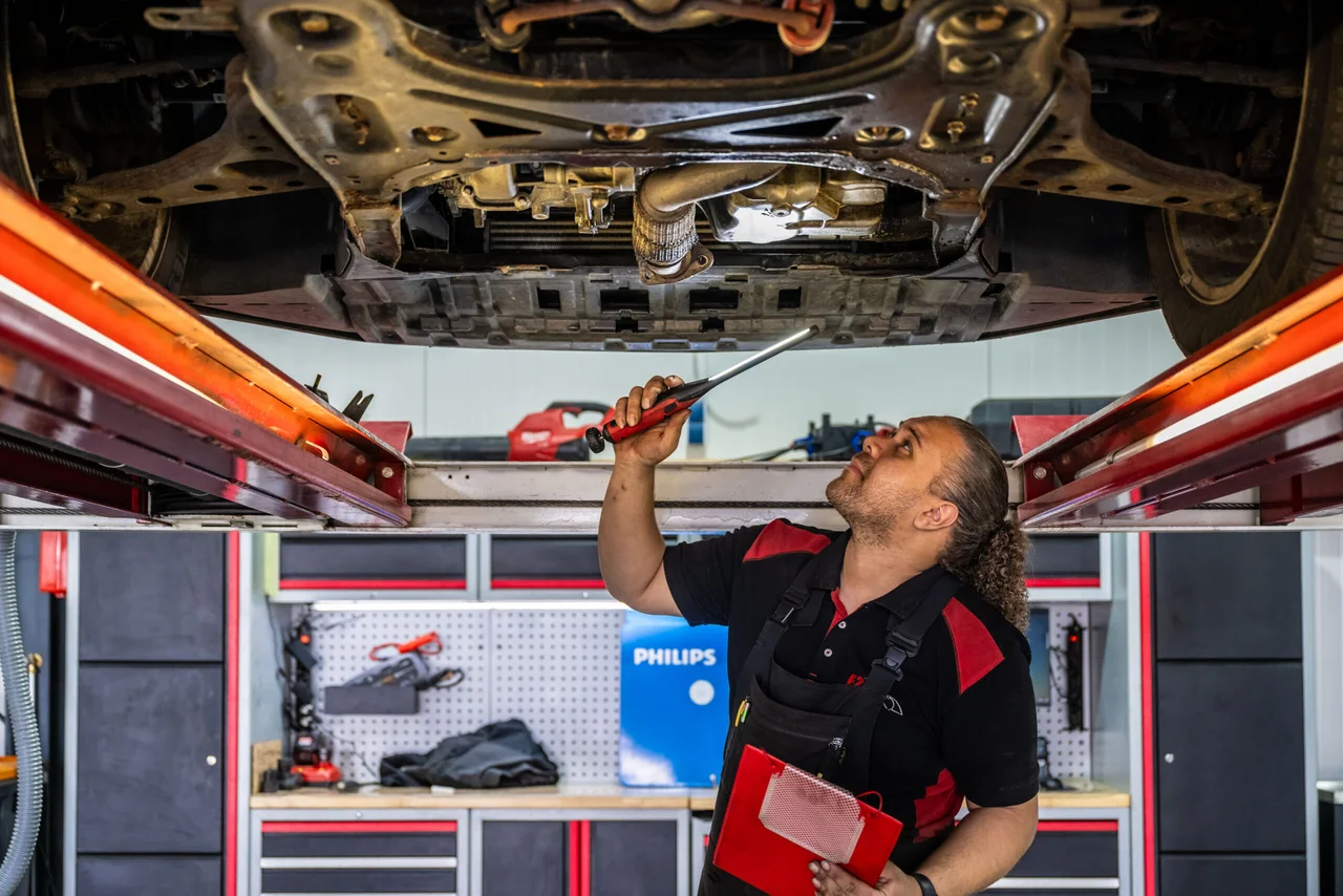 Механик FZ Auto’s работает под автомобилем на подъёмнике в мастерской.