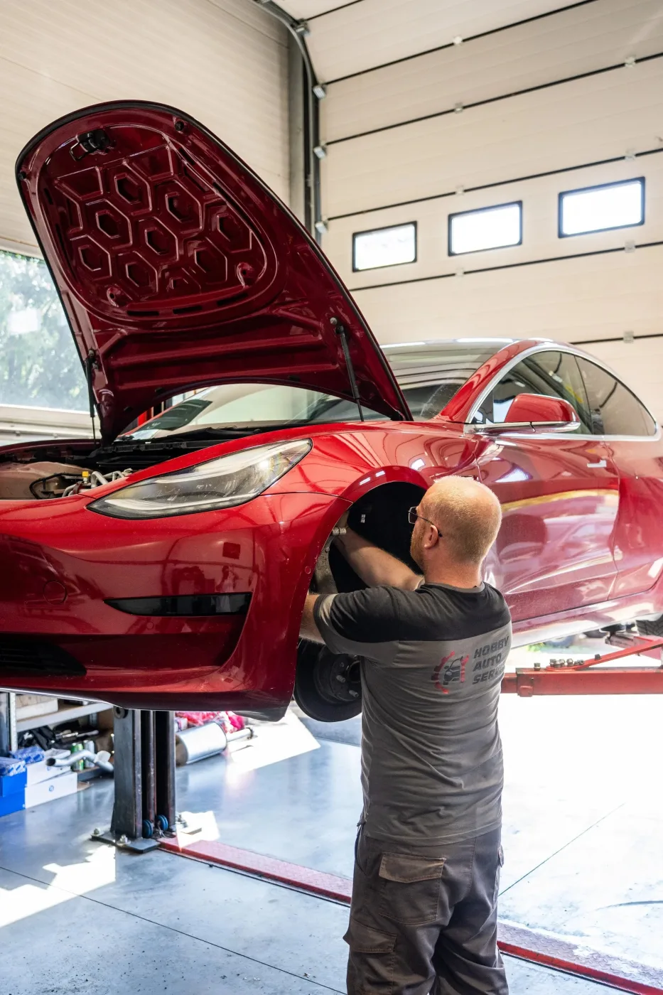 Механик HOBBY AUTO SERVIS обслуживает красную Tesla в мастерской.