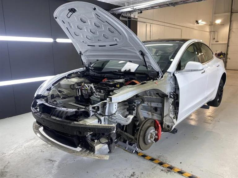 Белая Tesla со снятыми передними кузовными элементами в цехе HS Bílaréttingar og sprautun.