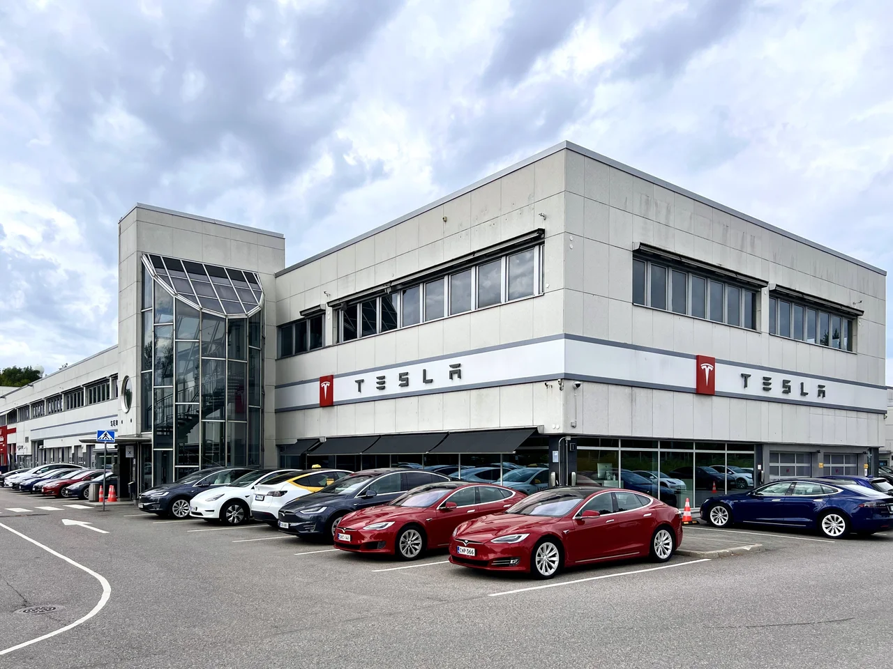 Фасад Tesla Center Helsinki-Vantaa с вывесками TESLA и припаркованными автомобилями по адресу Vetokuja 1. Снимок июля 2024 года.