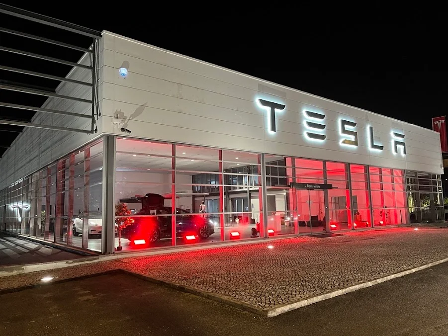 Фасад центра Tesla в Лейрии с подсвеченной вывеской и остеклённым входом.