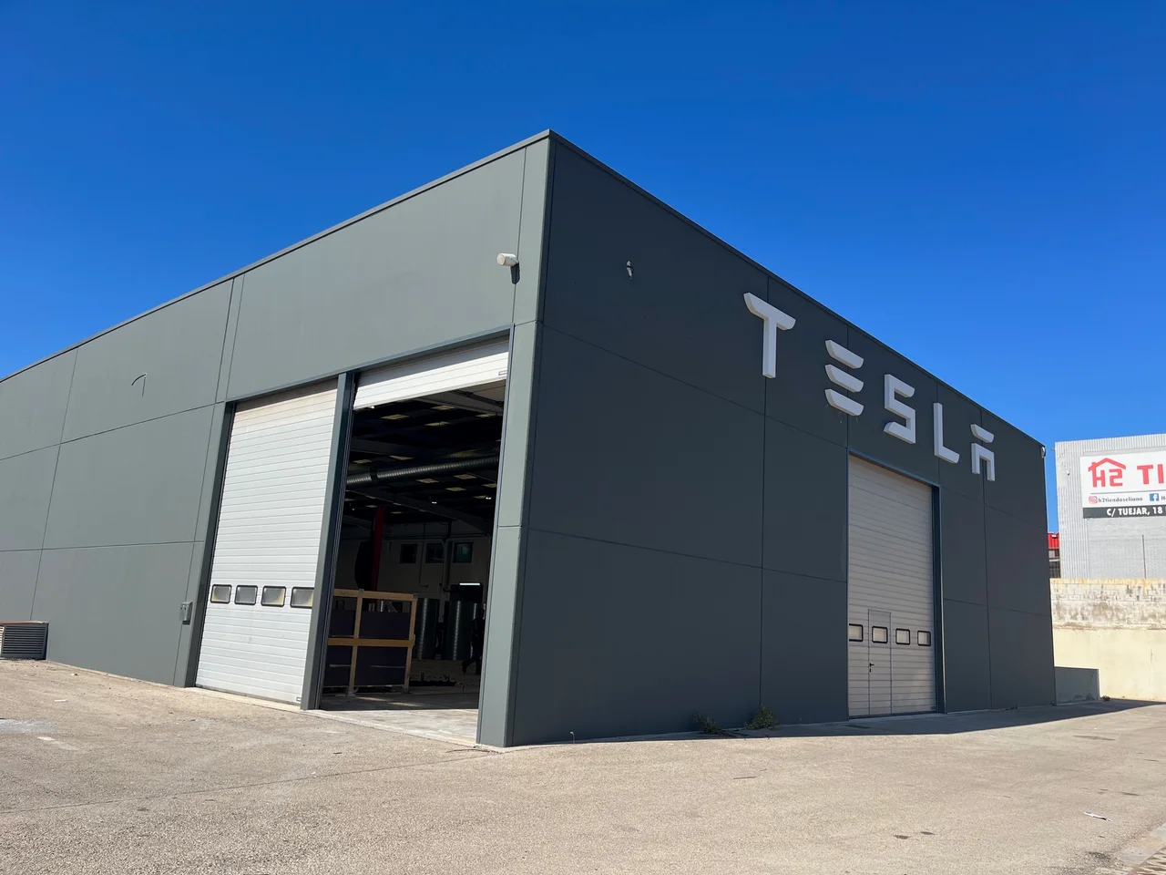 Фасад мастерской Tesla в Ла-Элиане, на котором виден логотип Tesla и въезд в производственные помещения.