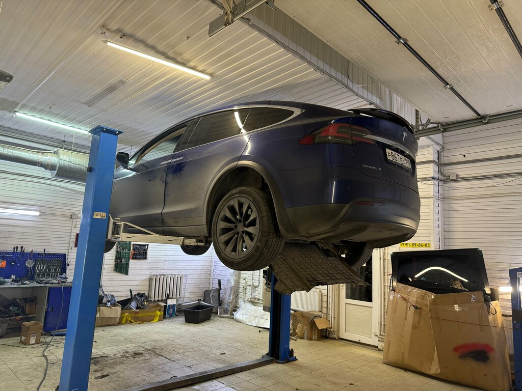 Tesla Model X поднята на подъёмнике в ремзоне с рабочим оборудованием.