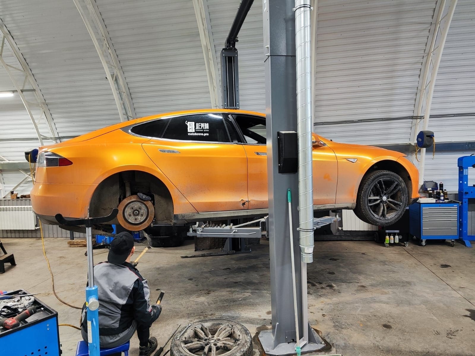 Tesla на подъёмнике в рабочем боксе Evolution Wings; специалист выполняет обслуживание.