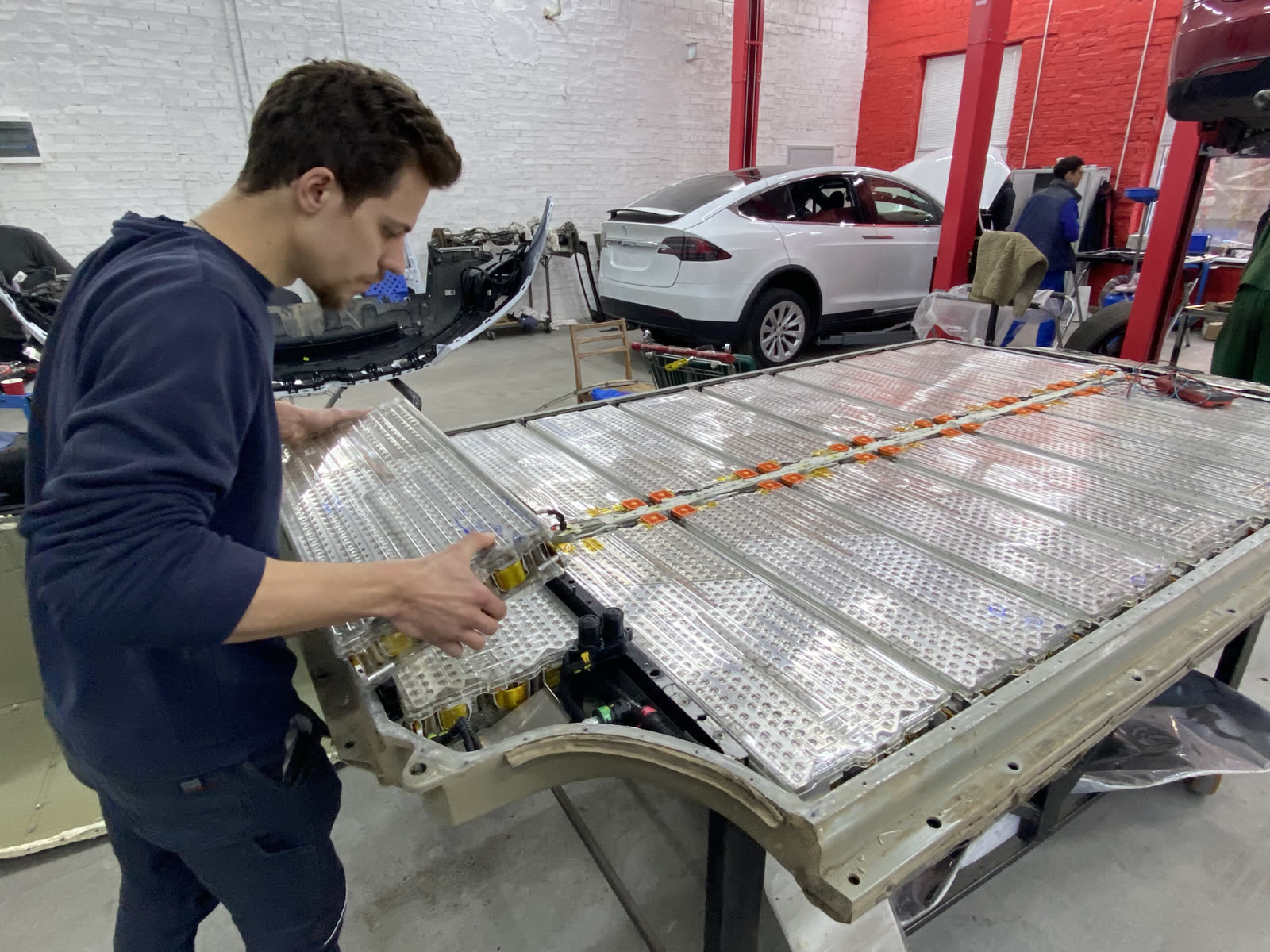 Work on an opened Tesla high-voltage battery in a service bay.