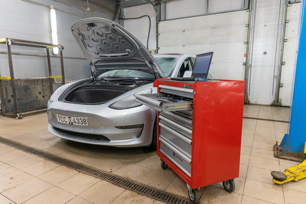 Tesla Model 3 в ремонтном боксе; капот открыт, рядом сервисное оборудование.
