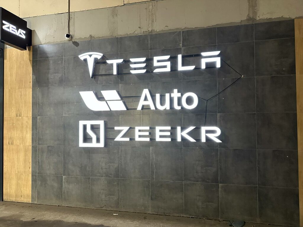 Интерьер сервисной зоны; на стене видны обозначения ZEVS, TESLA и ZEEKR.