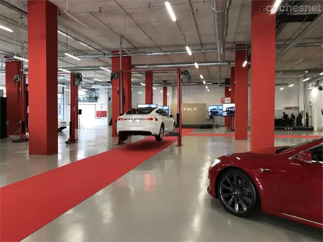 Interior del centro de servicio Tesla de la calle Metal·lúrgia, en Barcelona, con un automóvil en un elevador y varios puestos de trabajo.
