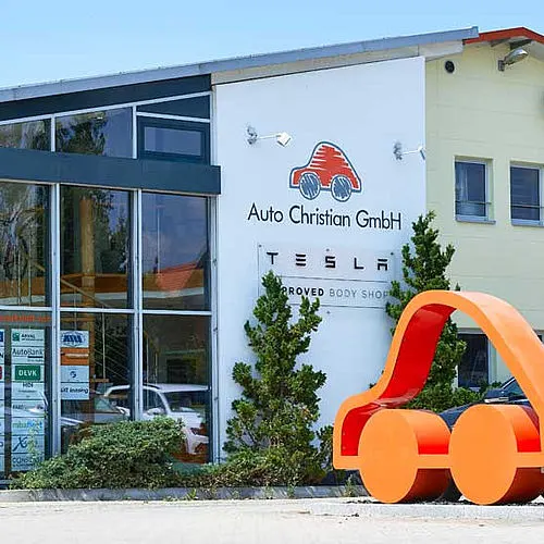 Gebäude von Auto Christian in Oberpframmern mit einem Schild „Tesla Approved Body Shop“.