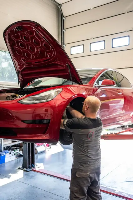 Mechanik HOBBY AUTO SERVIS opravuje v dielni červenú Teslu.