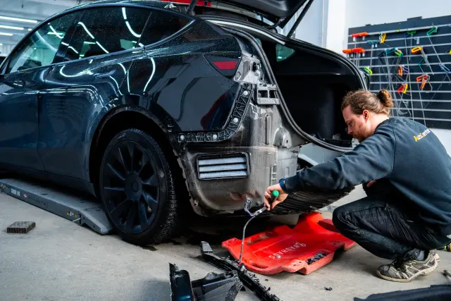 Starfsmaður AutoCenter vinnur að afturhluta Tesla-bifreiðar á yfirbyggingarverkstæðinu.