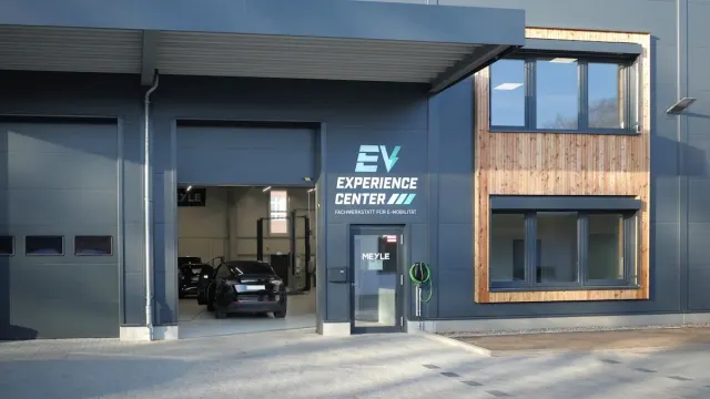 Außenansicht der Werkstatt des EV Experience Center; die Tore sind geöffnet und ein Auto steht im Inneren.